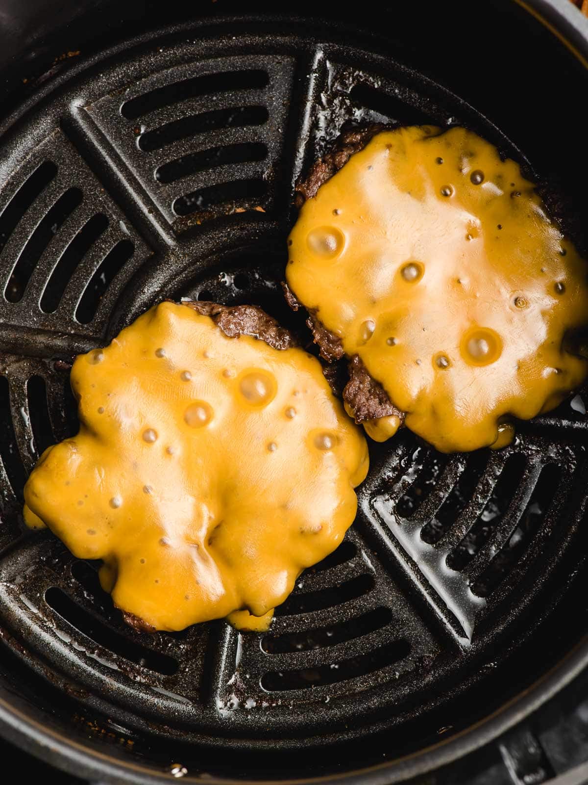 Two air fryer hamburgers covered in melted cheese.