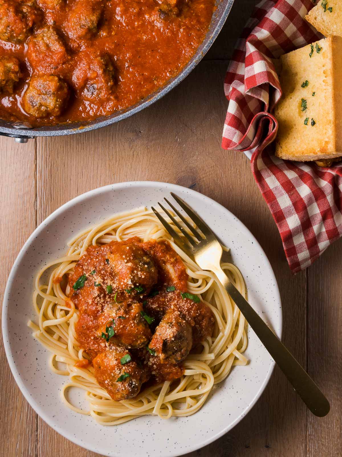 A plate of spaghetti with gluten free meatballs and a basket of garlic bread on a table.
