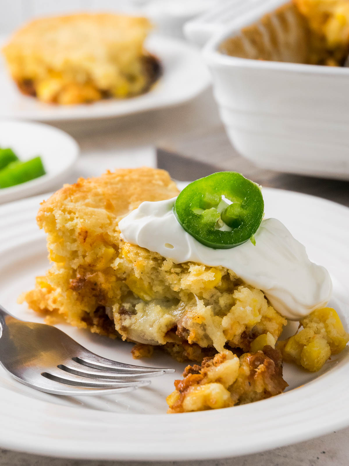A slice of Mexican cornbread casserole with ground beef topped with sour cream on a plate with a fork.