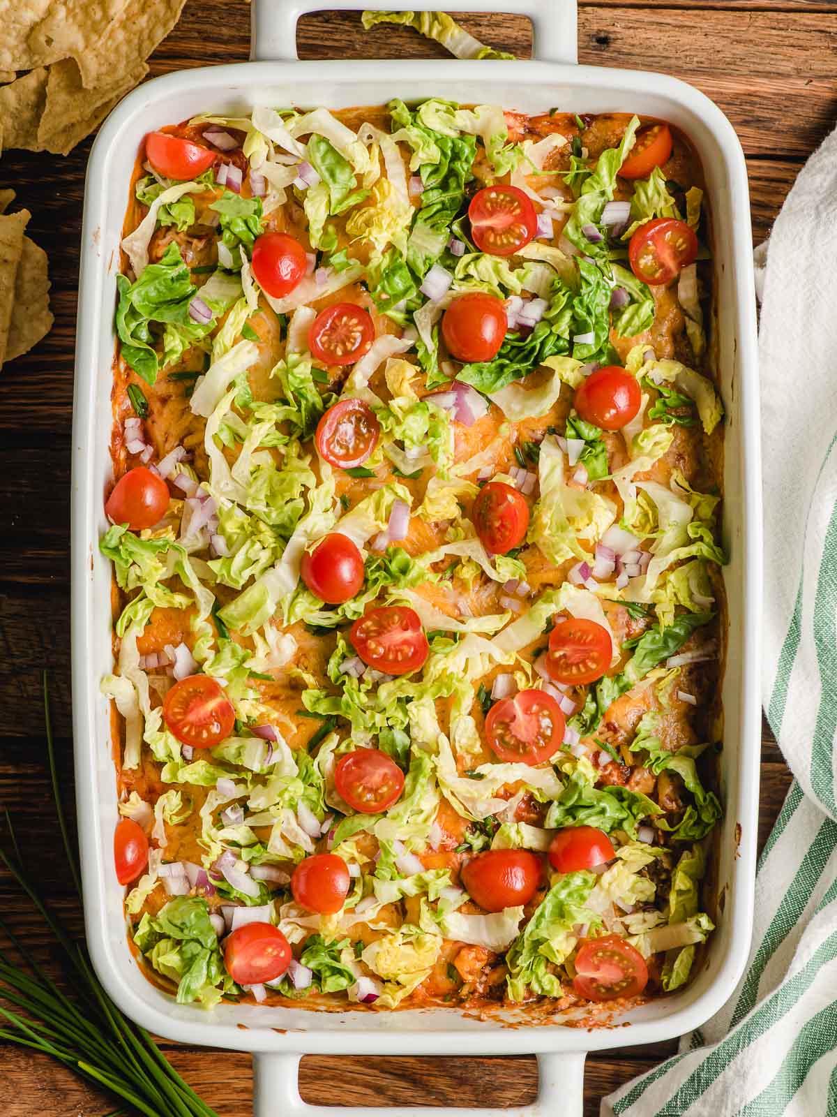 A serving dish filled with baked layered taco dip, topped with tomatos and lettuce
