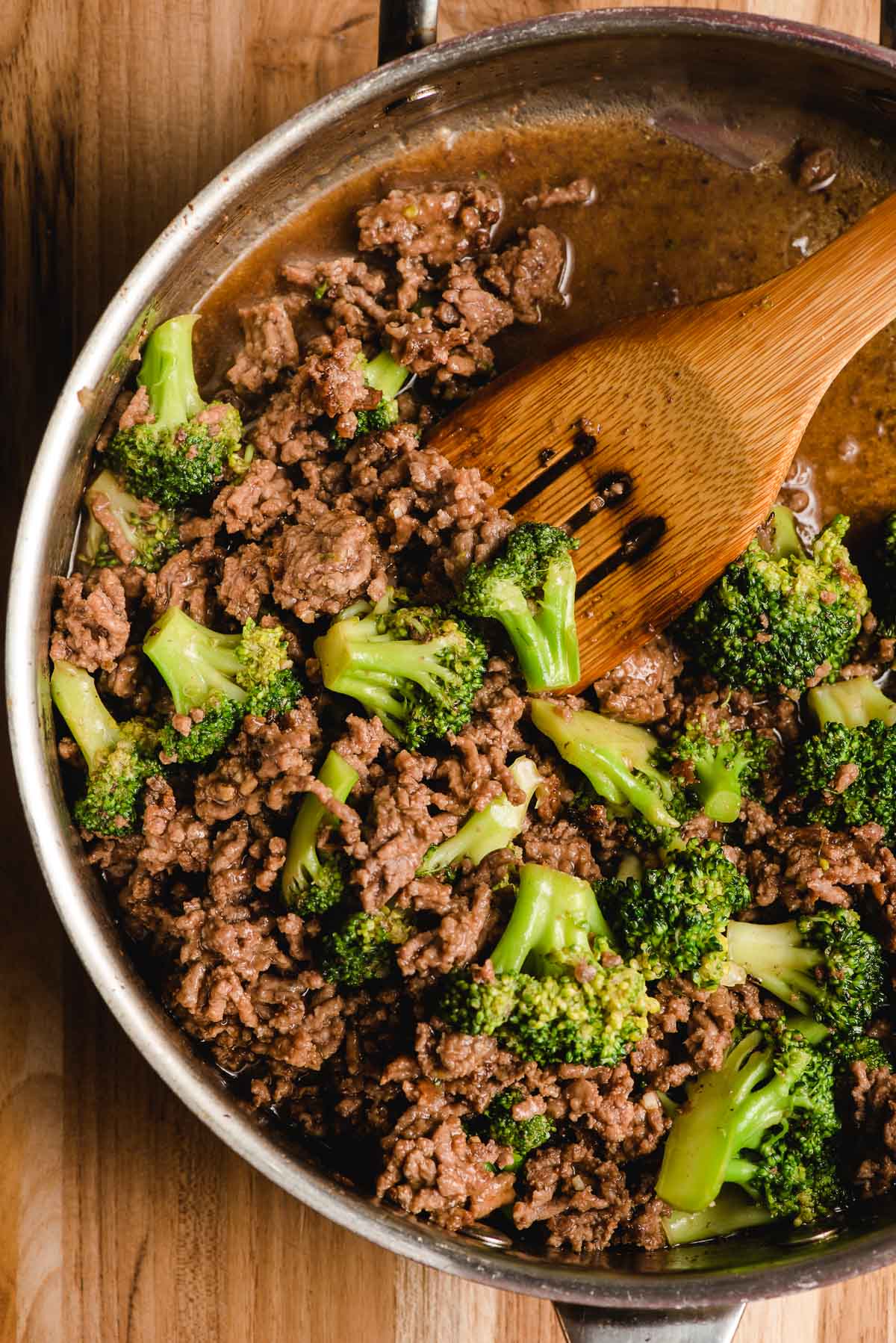 Wooden spatula scooping ground beef and broccoli.