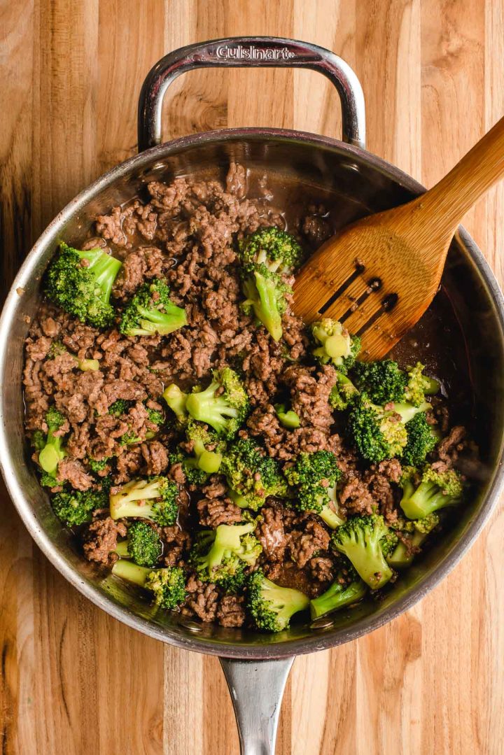 Broccoli and ground beef in a skillet with a wooden spatula.