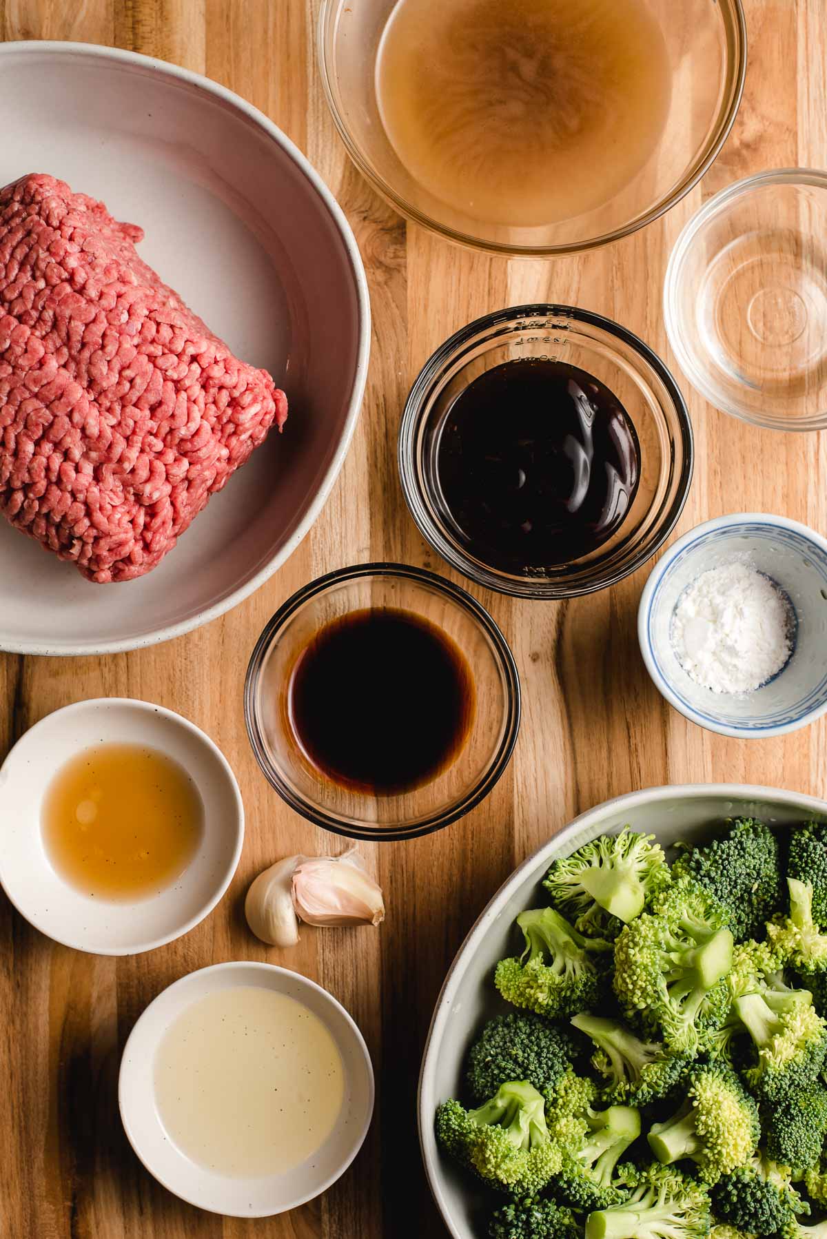 Ingredients displayed on a wood background--ground beef, oyster sauce, soy sauce, beef broth, mirin, garlic, broccoli and sesame oil,. 