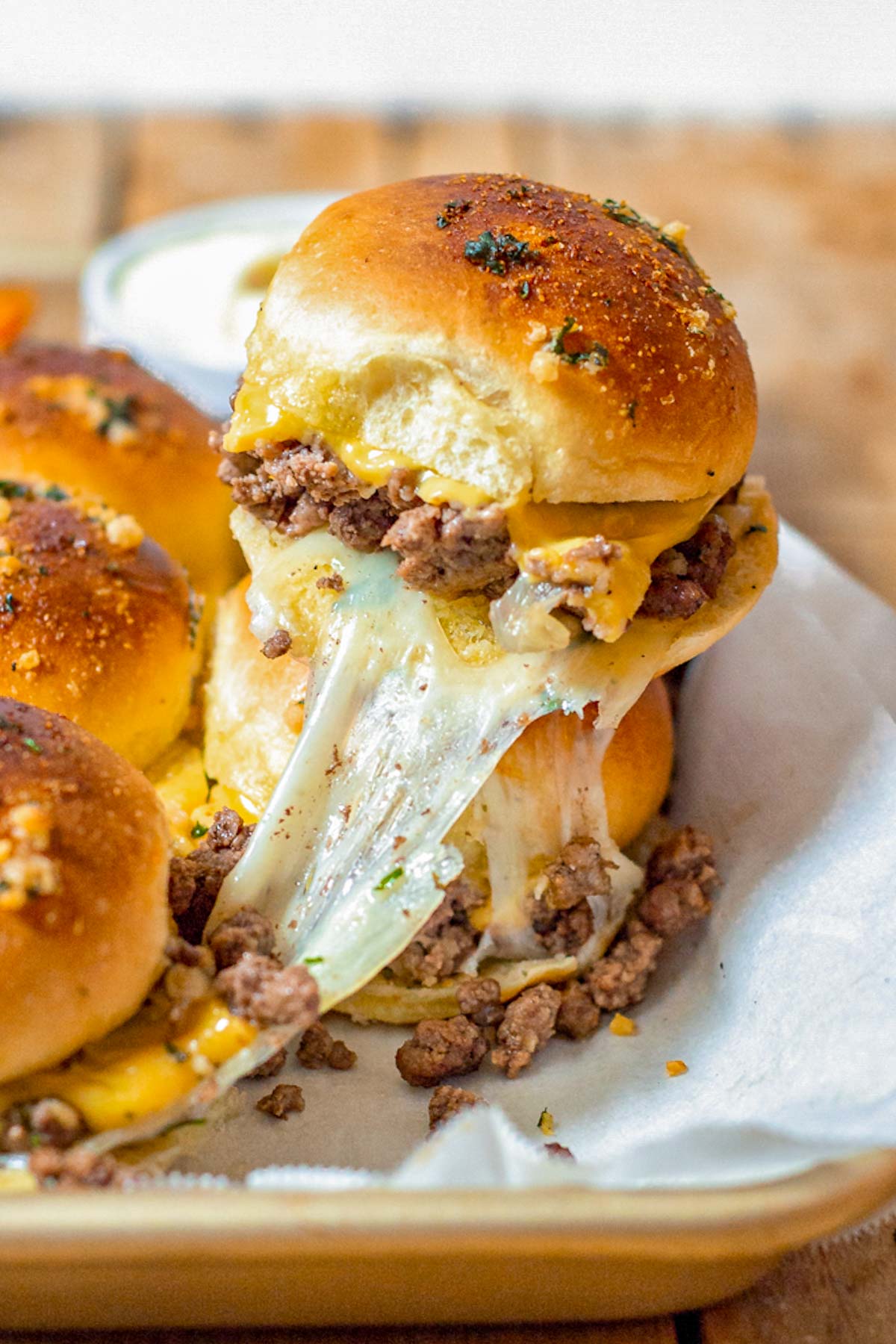 Cheese stretches as a Ground Beef Slider is pulled from a baking tray.
