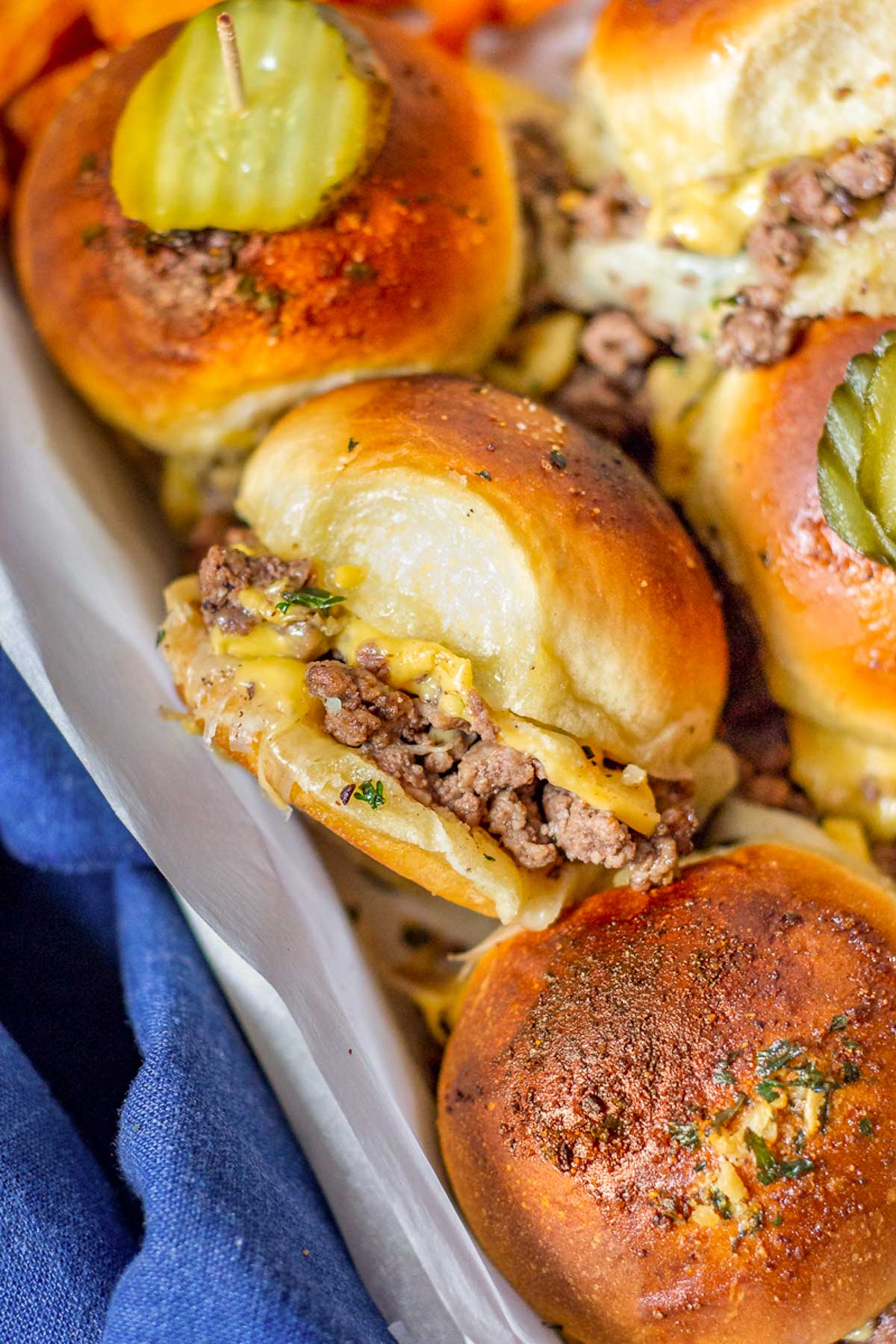 A cooked tray of Ground Beef Sliders topped with pickle.