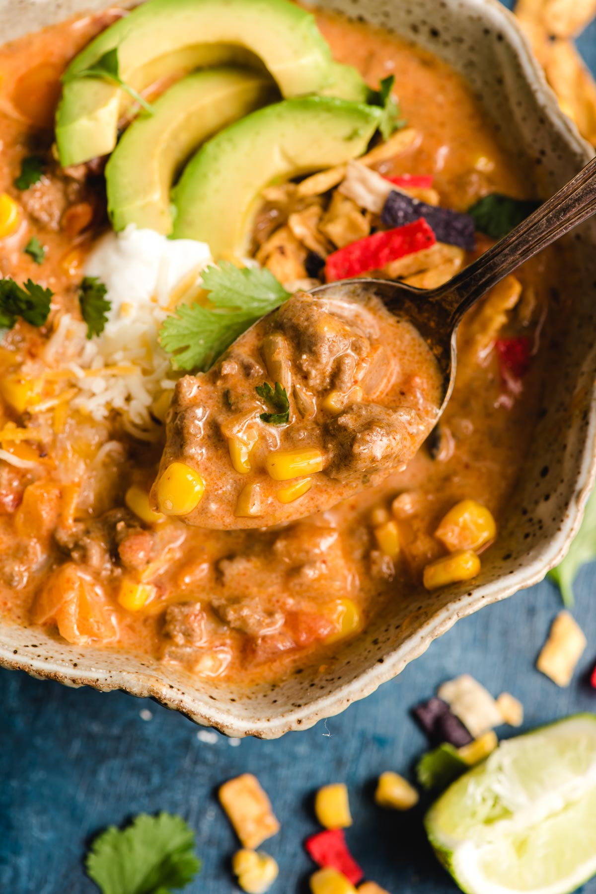 Spoonful of ground beef enchilada soup with corn, cilantro, cheese, and lime.