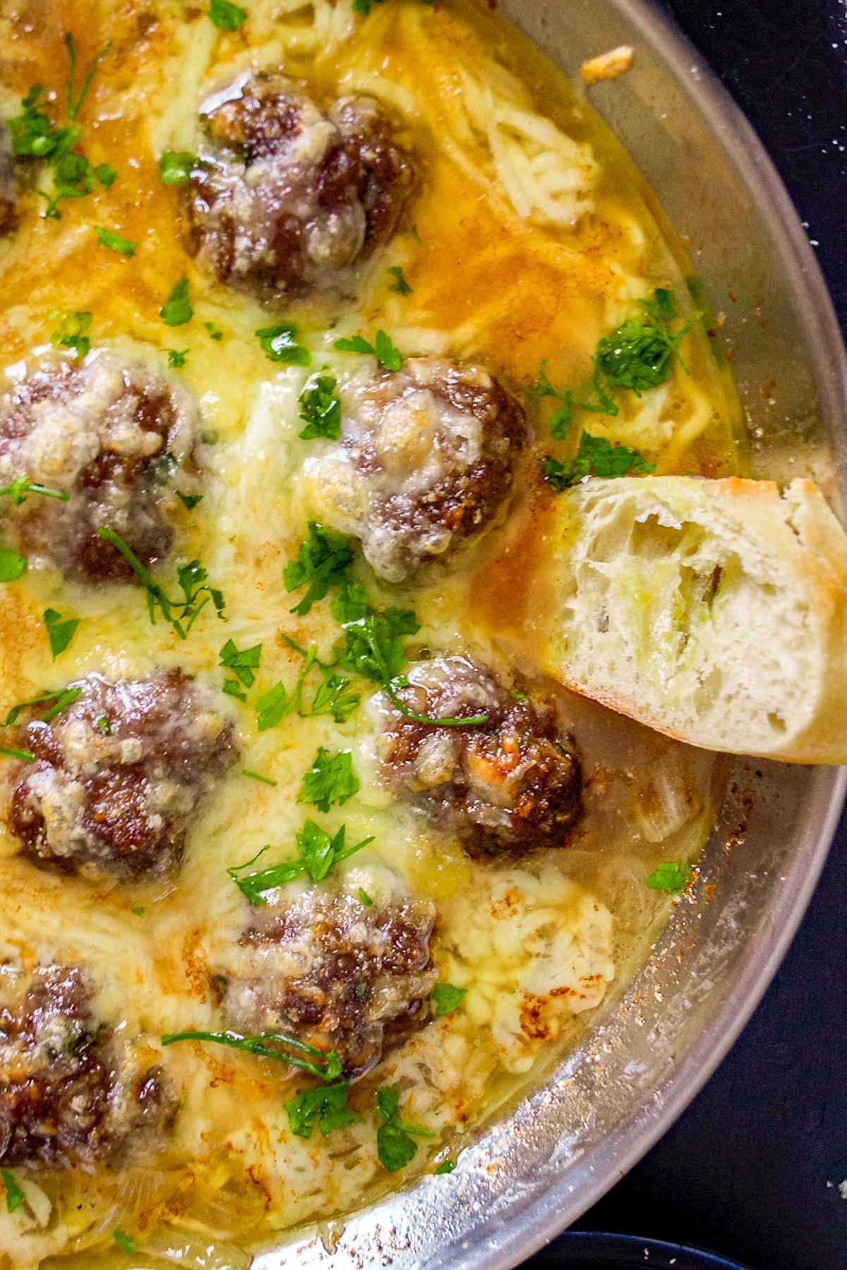 A slice of bread in a pan of french onion soup with meatballs.