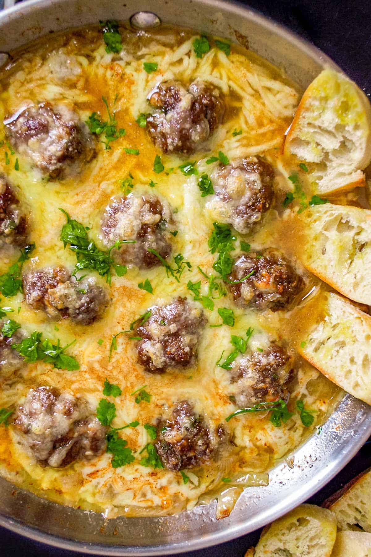 A skillet full of cheesy meatballs with toasted bread.
