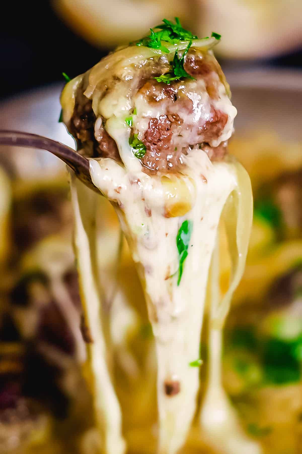 Melted cheese drips off a spoon holding a meatball.