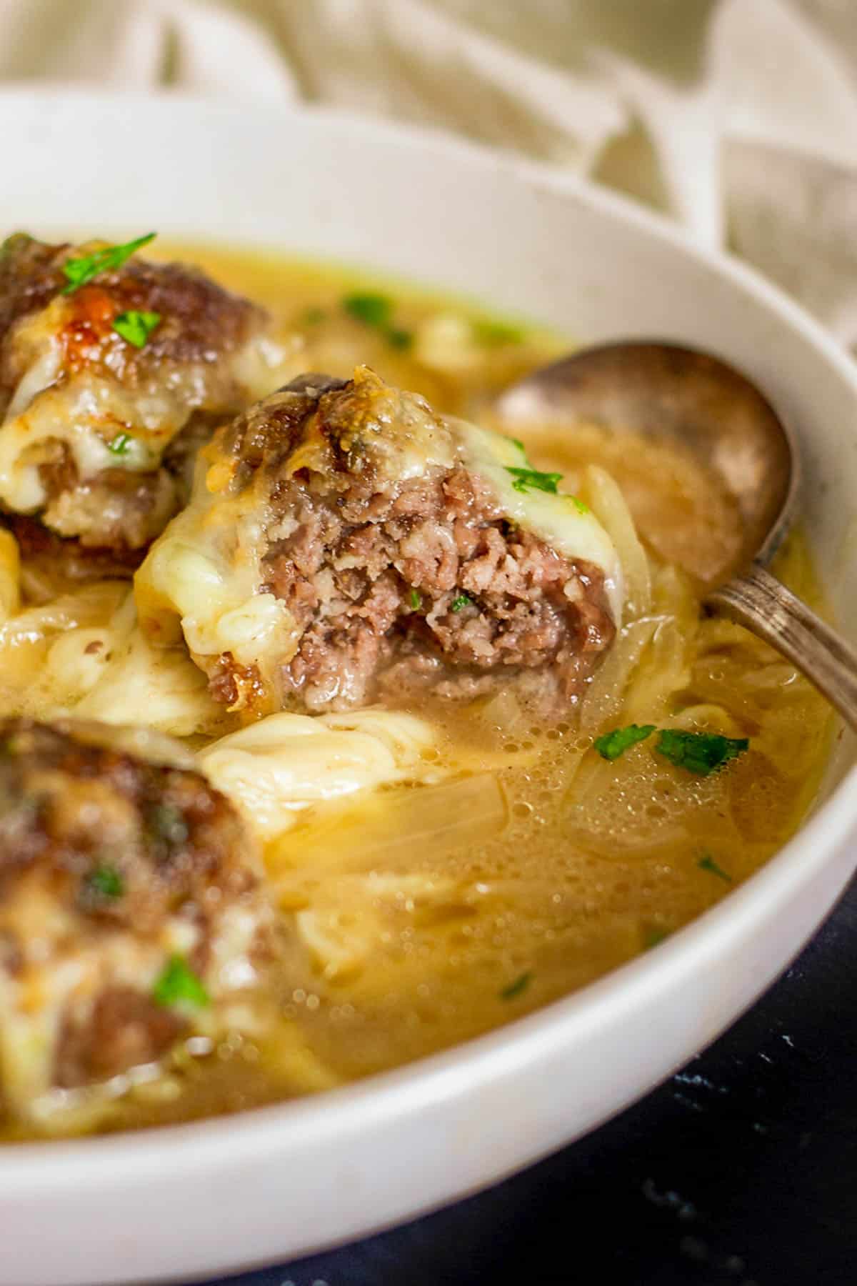 A cheese-topped meatball in a bowl of soup.