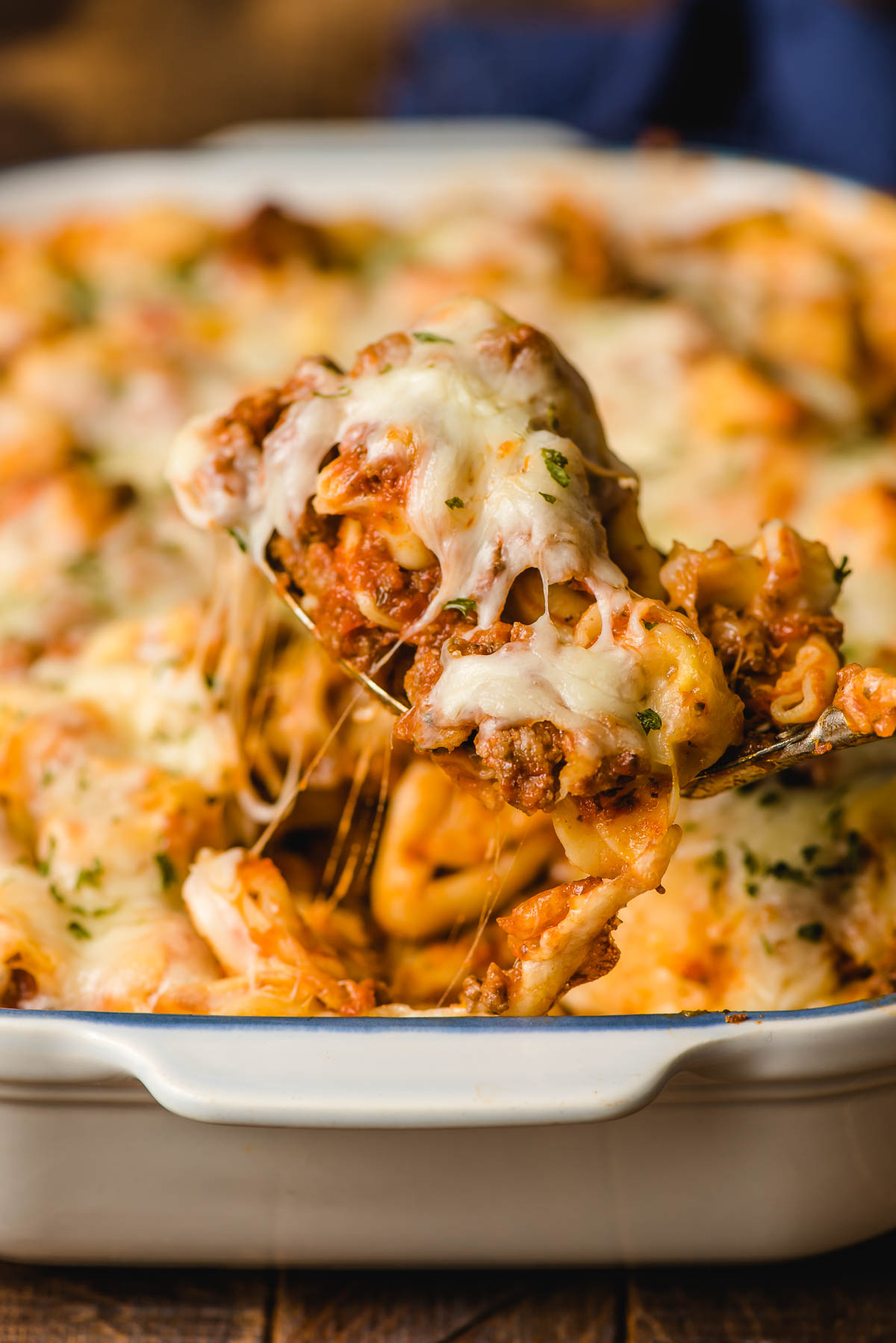 Cheesy tortellini bake in a serving spoon over a casserole dish.