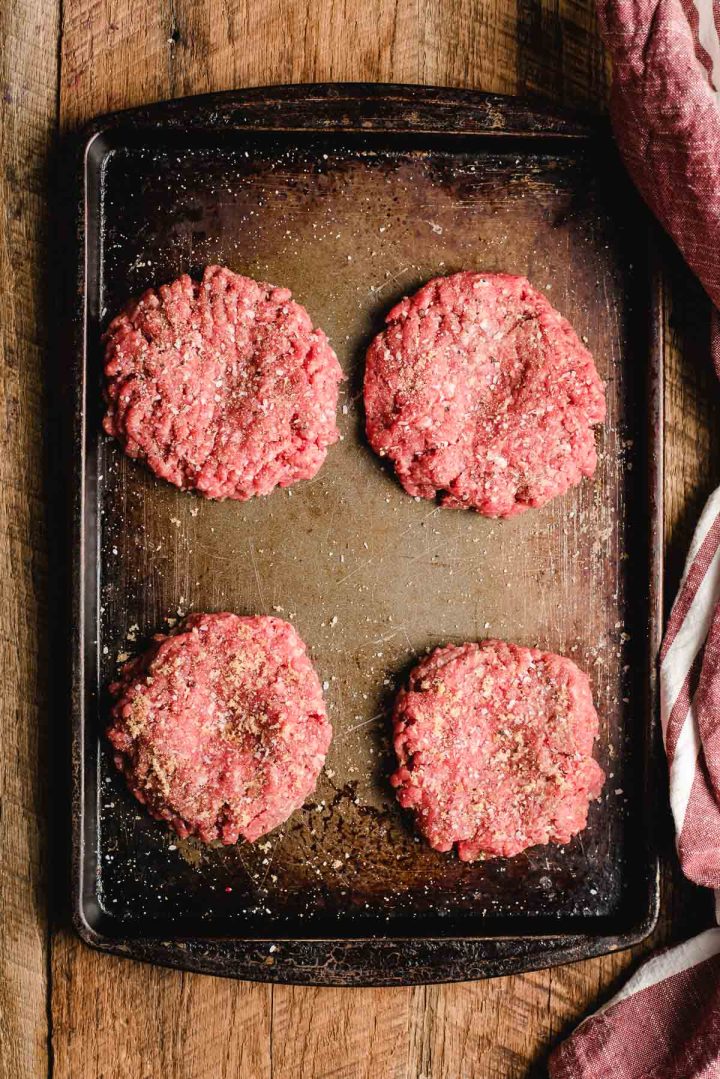 Four burger patties on a sheet pan.