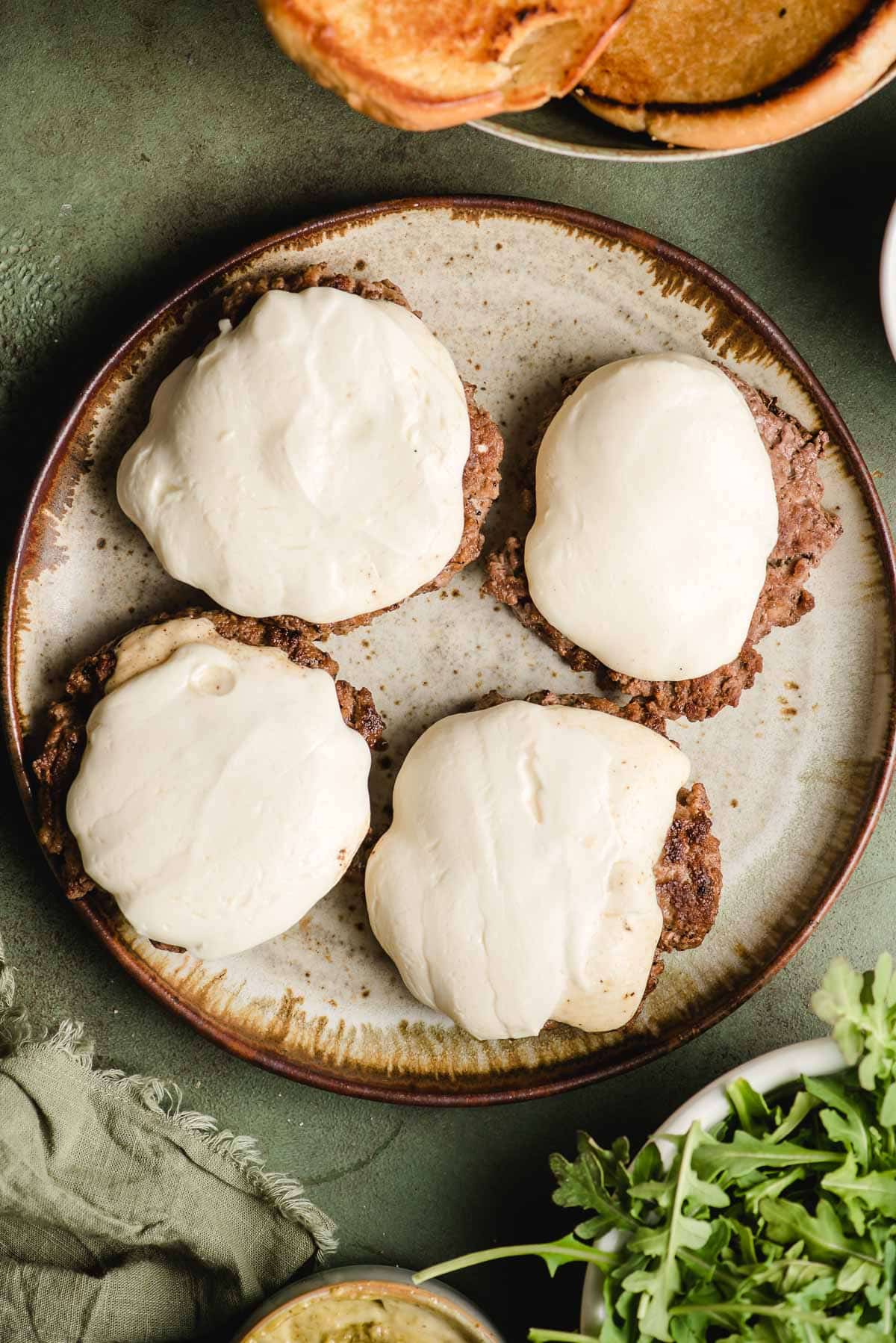Four ground beef burger patties topped with melted mozzarella sit on a plate.