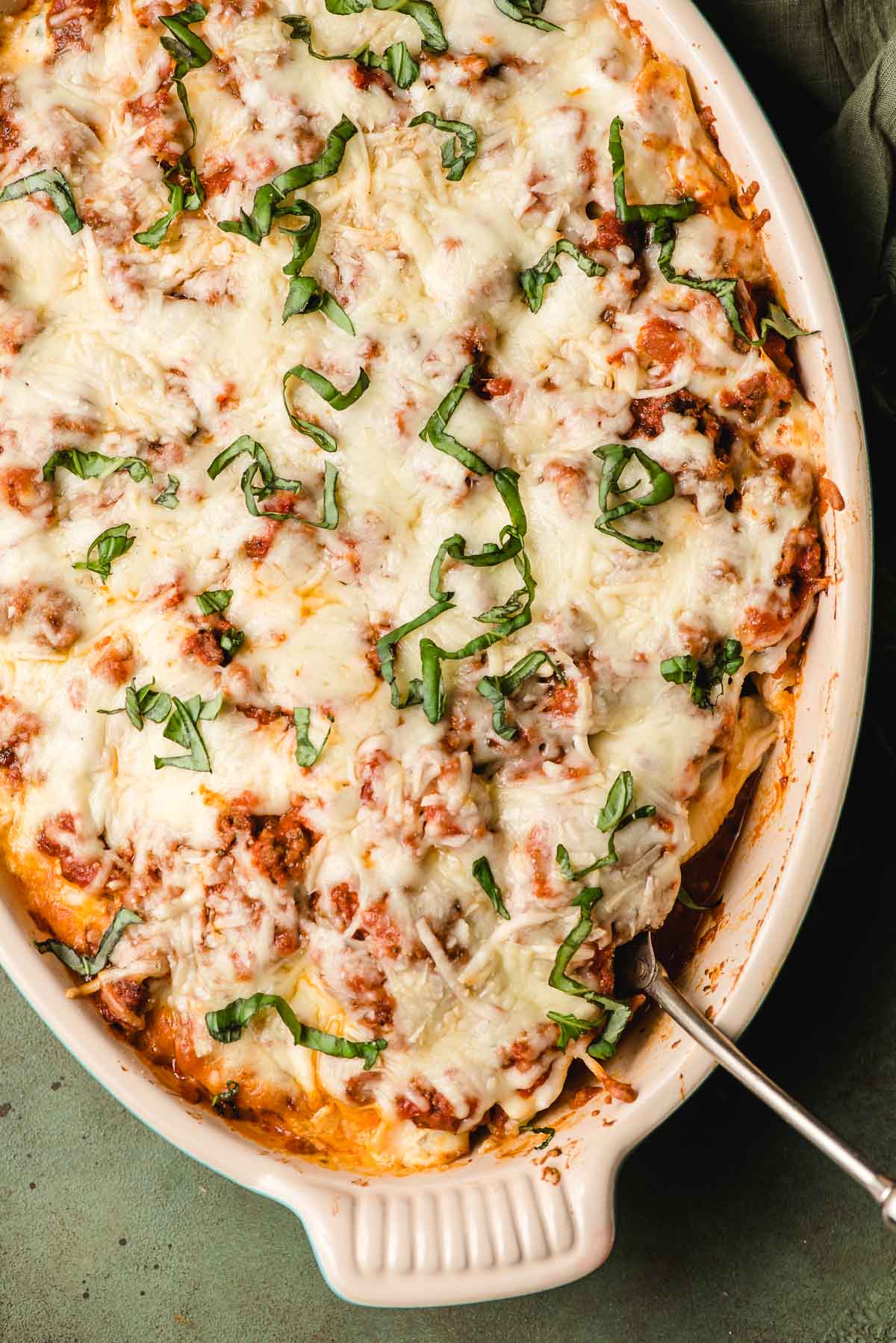 A colorful baking dish of cottage cheese stuffed shells with ground beef is topped with fresh basil.