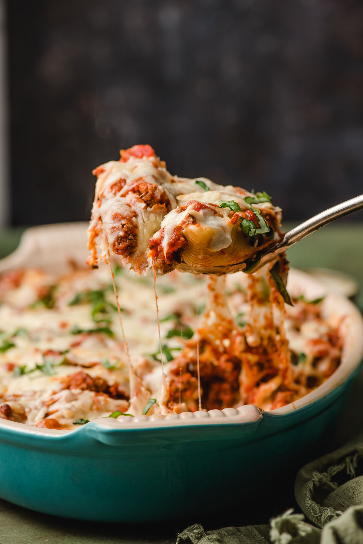 Melted cheese stretches from a scoop of stuffed shells with ground beef.
