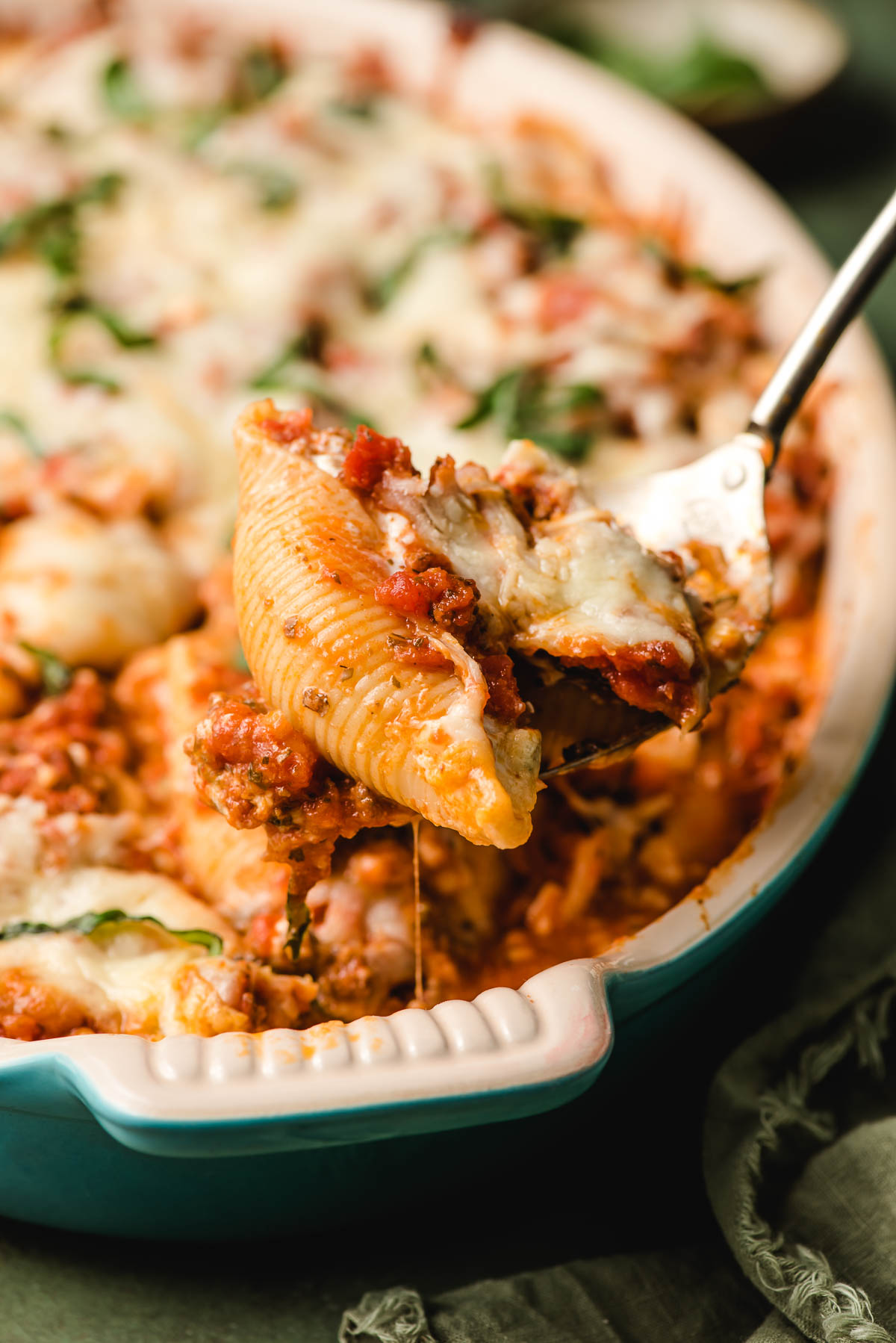 A spoon scoops Cottage Cheese Stuffed Shells from a baking dish.