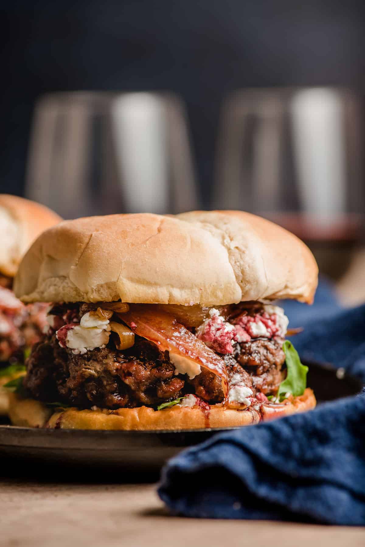 Goat cheese burger on a plate with red wine glasses in the background.