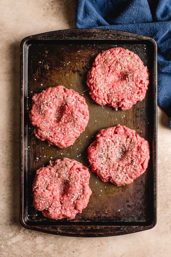 Hamburger patties on a sheet pan with a thumb indent in the middle of each one.