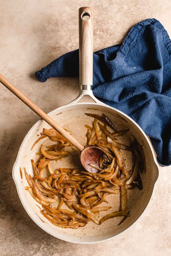 Caramelized onions in a skillet stirred with a wooden spoon.