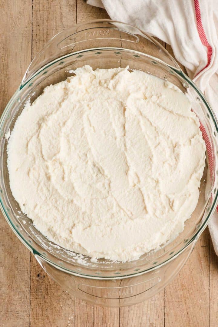 Ricotta cheese spread on the bottom of a glass pie plate.