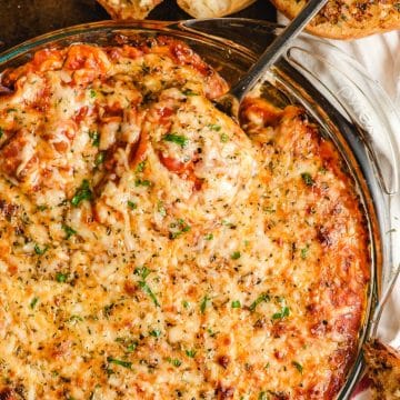 Cheesy baked lasagna dip with a metal spoon dipping in.