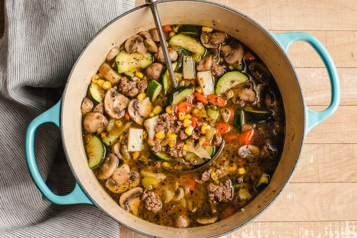 Dutch oven full of vegetables, broth, and ground beef, with seasoning.