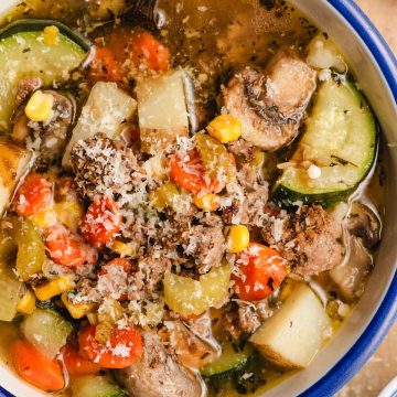 Bowl of vegetable soup with ground beef, sprinkled with Parmesan cheese.