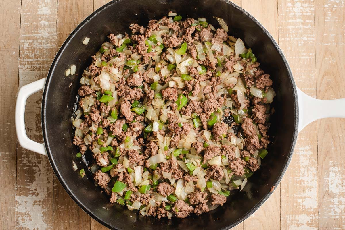 Skillet with sauteed ground beef, onions, and green bell peppers.