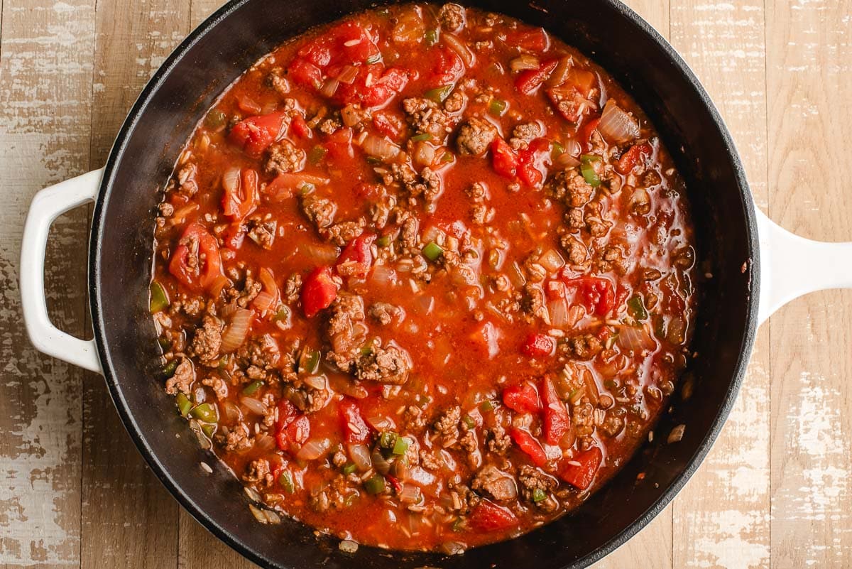 Skillet full of hamburger, onions, peppers, beef broth, diced tomatoes, and rice.