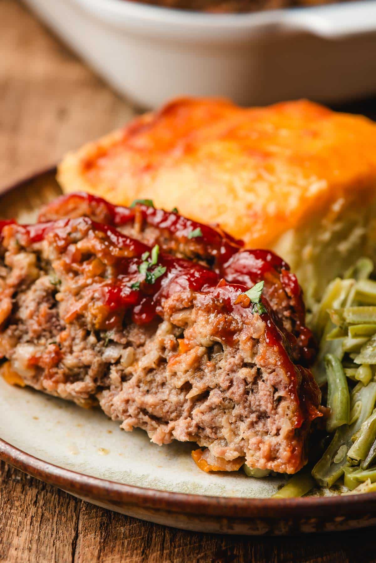 Slices of ketchup glazed meatloaf with cheesy potatoes and green beans on a plate.