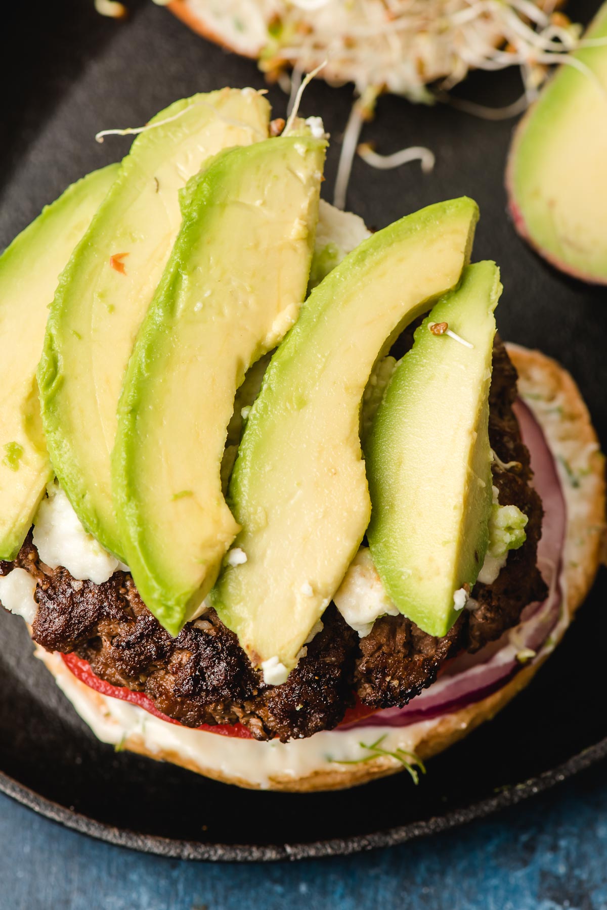 Open face burger with slices of avocado.
