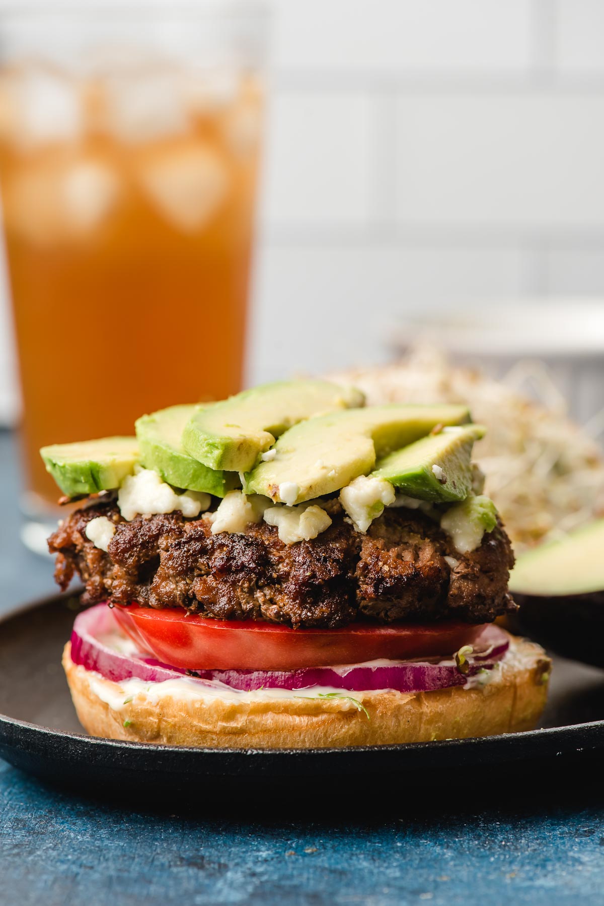 Open face burger stacked with tomato, red onion, queso fresco, and avocado.