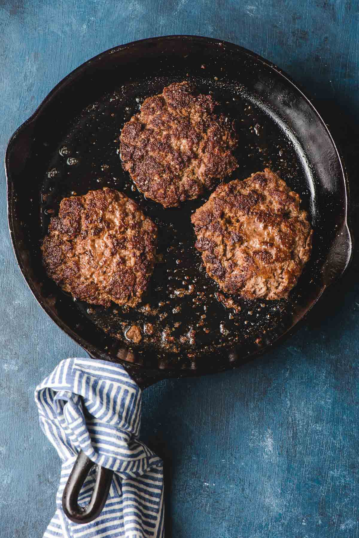 3 burger patties in a cast iron skillet.