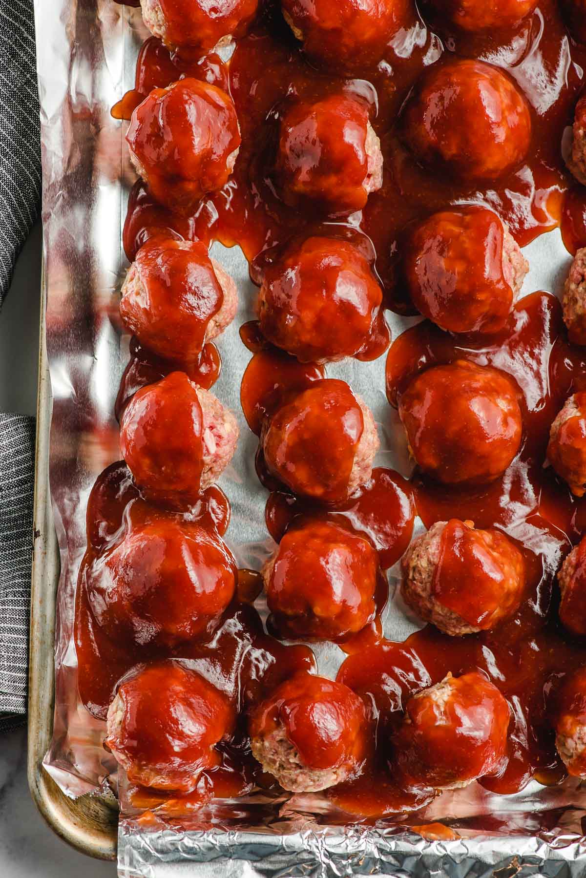 Unbaked meatballs covered in barbecue sauce on a baking tray.