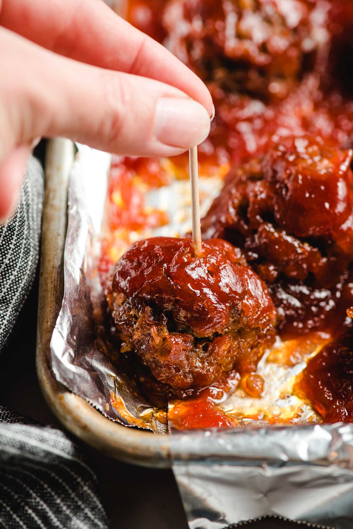 Finger picking up a barbecue meatball with a toothpick.