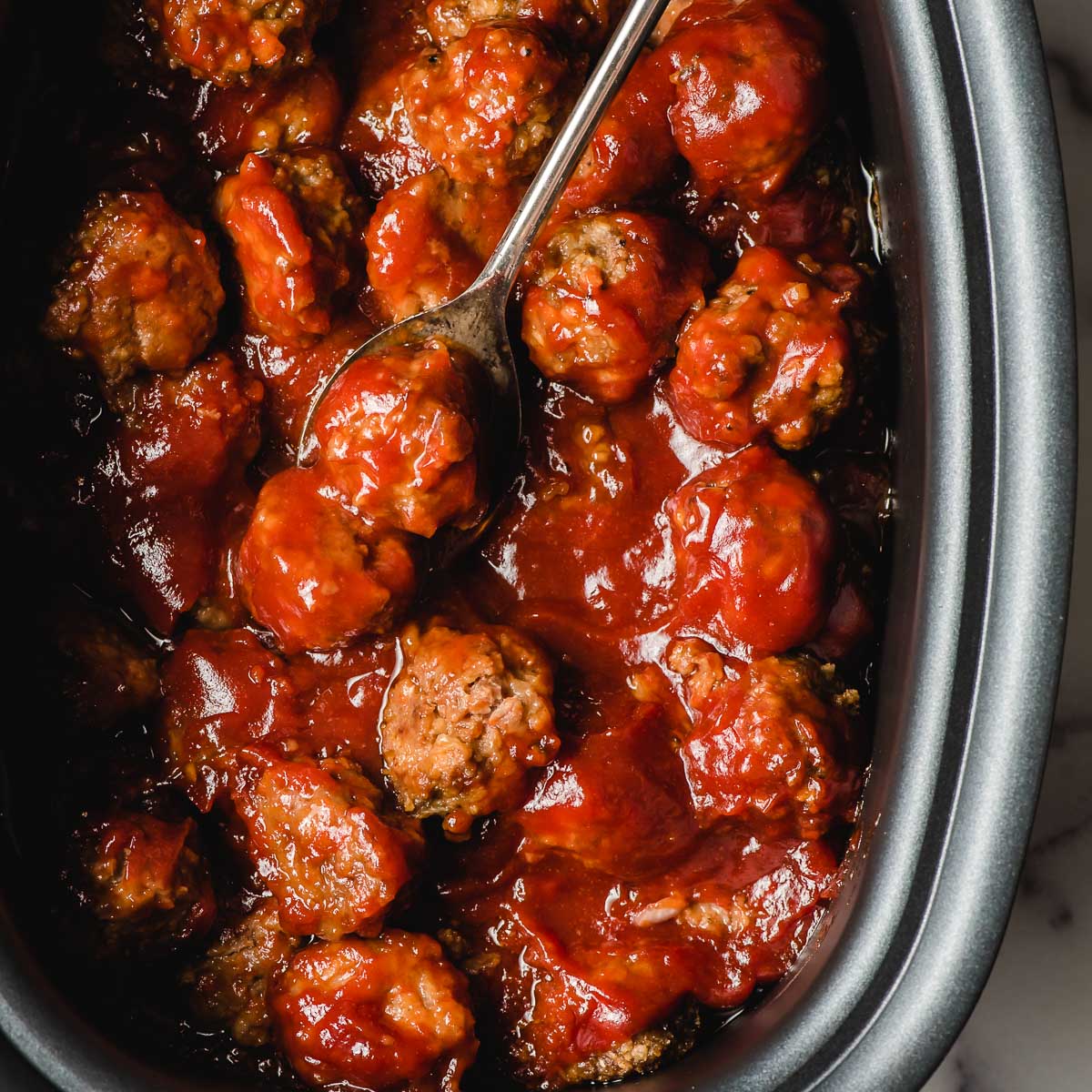 BBQ Meatballs for a party shown in a crock pot with a metal spoon.