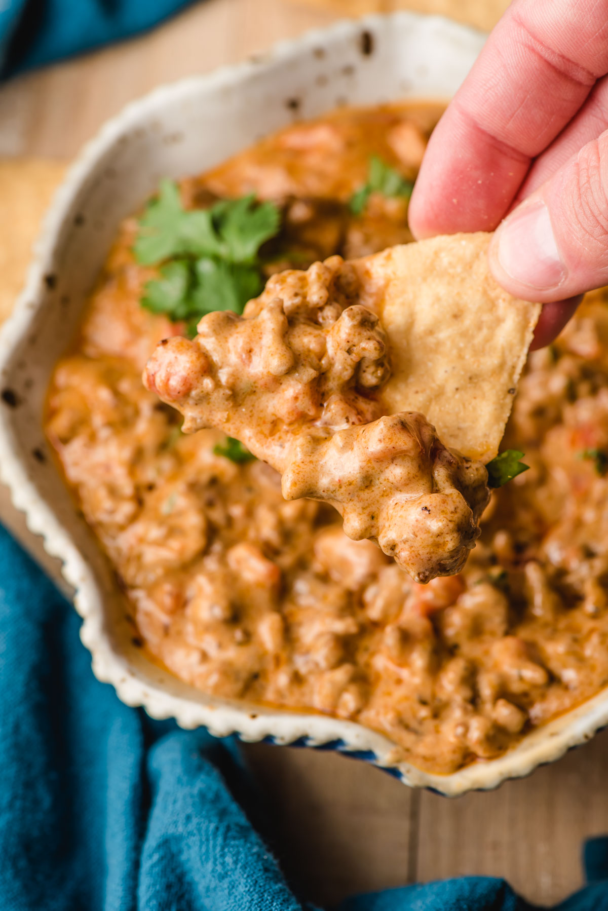 A hand dips a tortilla chip into a bowl of queso dip with meat.