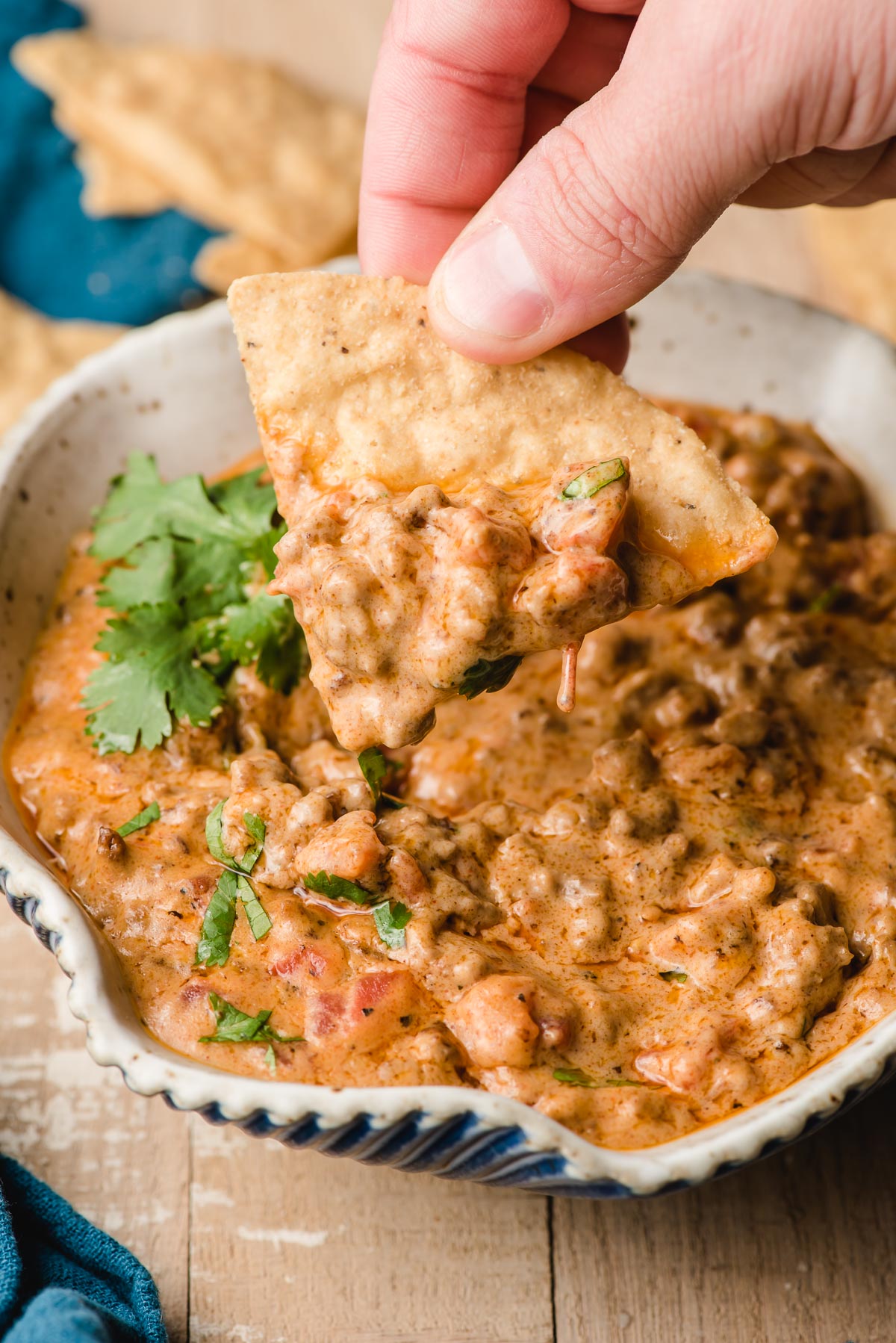 A chip takes a dip of ground beef queso out of a bowl.