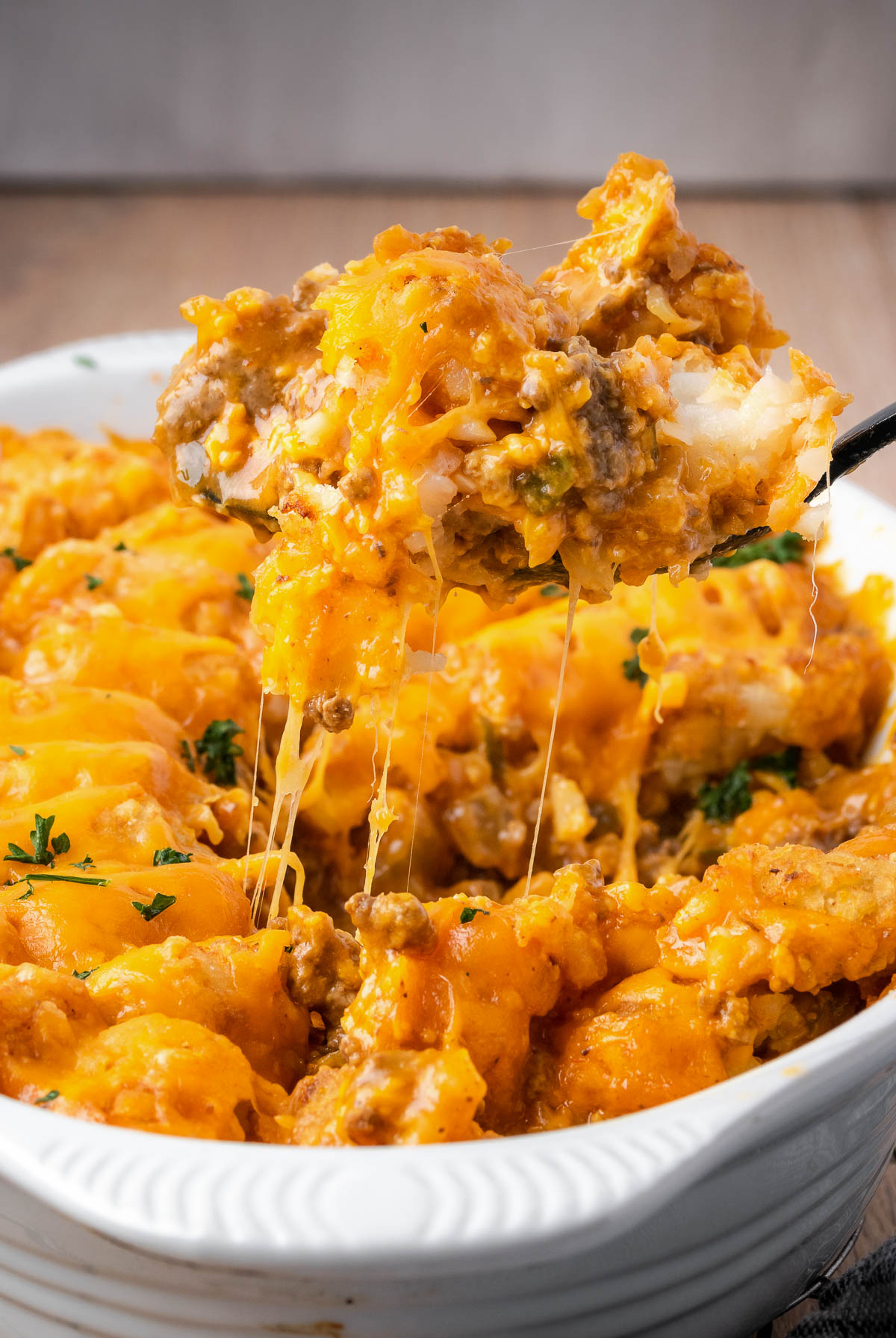 A cheesy serving of Cheeseburger Tater Tot Casserole is lifted from a casserole dish.