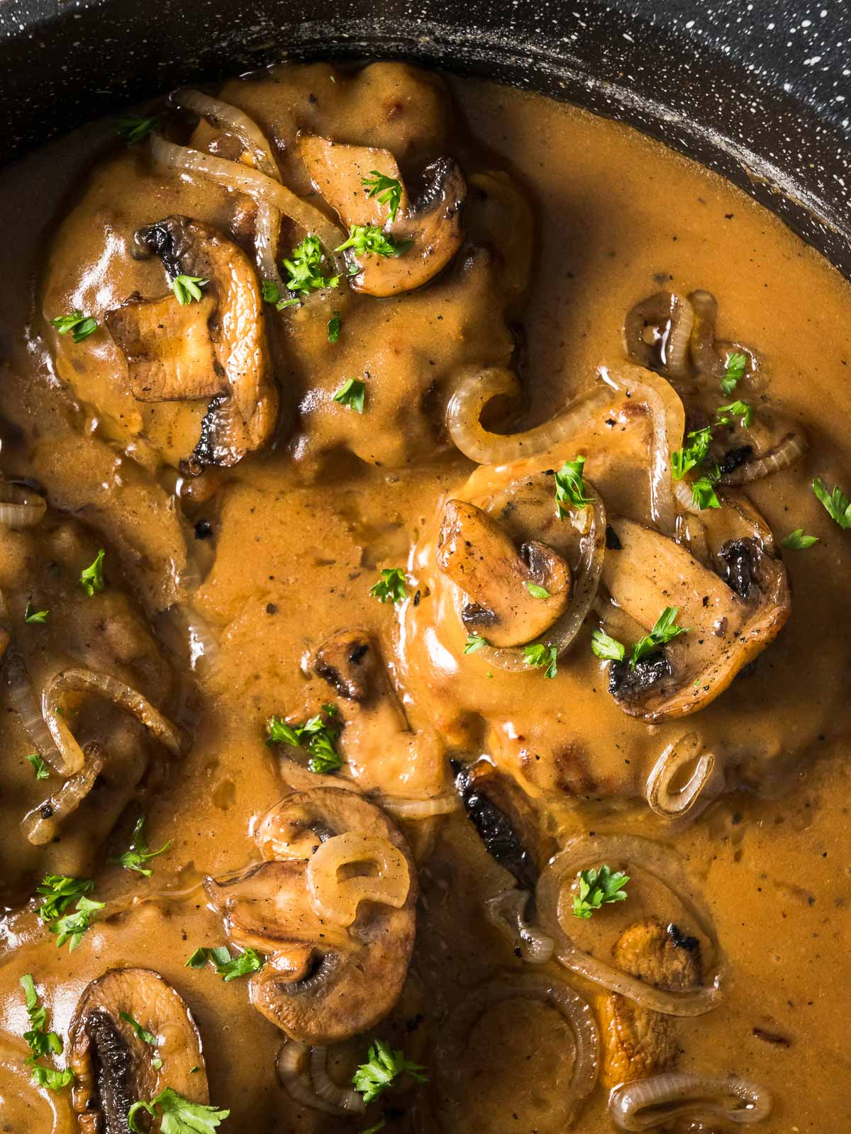Smothered Chopped Steaks simmer in a skillet with gravy, onions, mushrooms, and herbs.