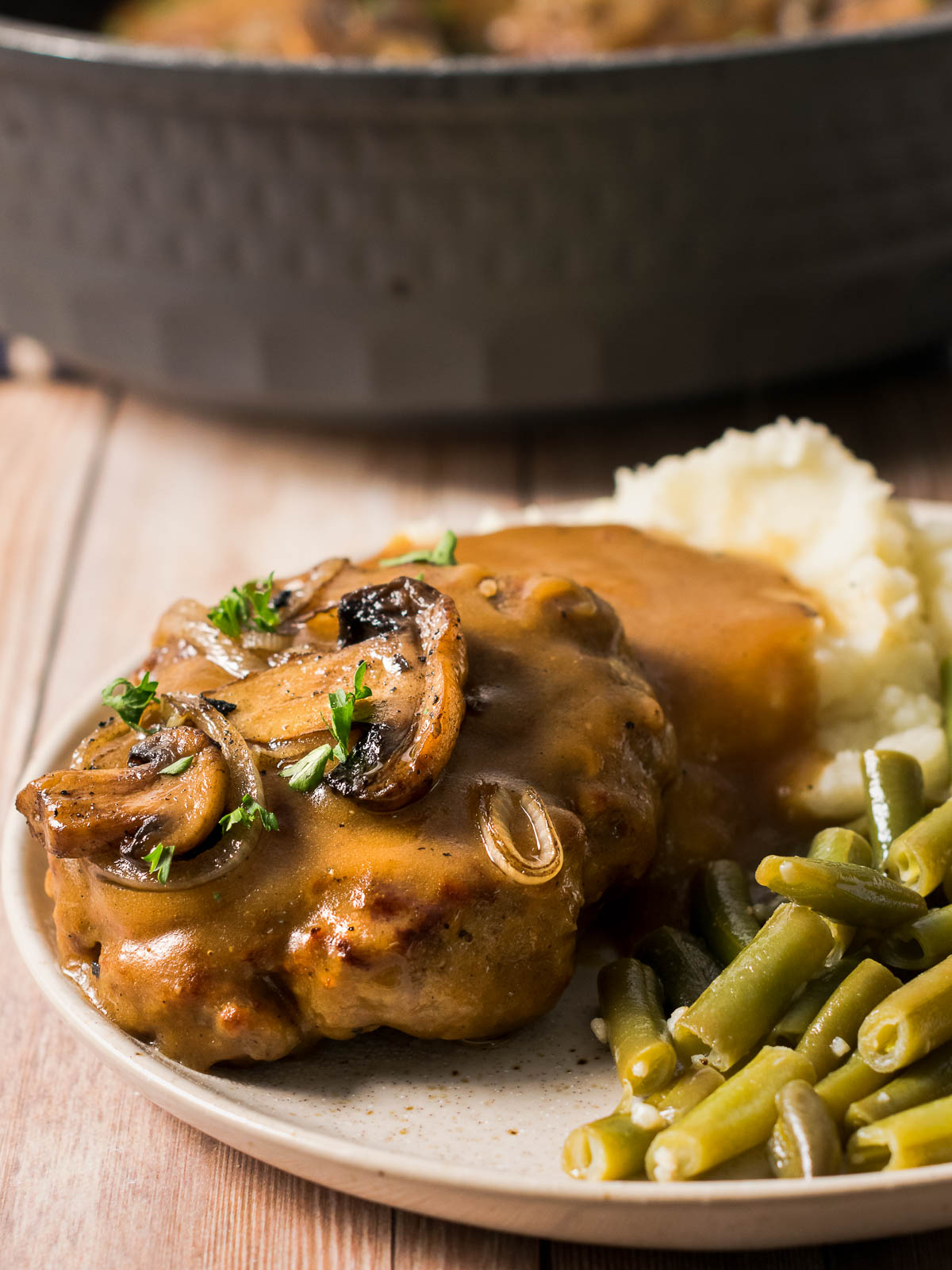 Chopped steak and gravy on mashed potatoes served on a plate with green beans.