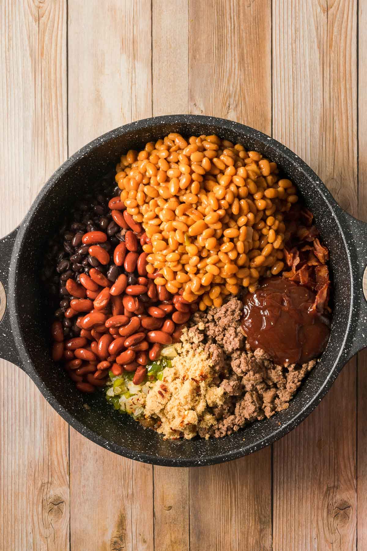 All the ingredients for cowboy baked beans with ground beef ready to cook in a pot.