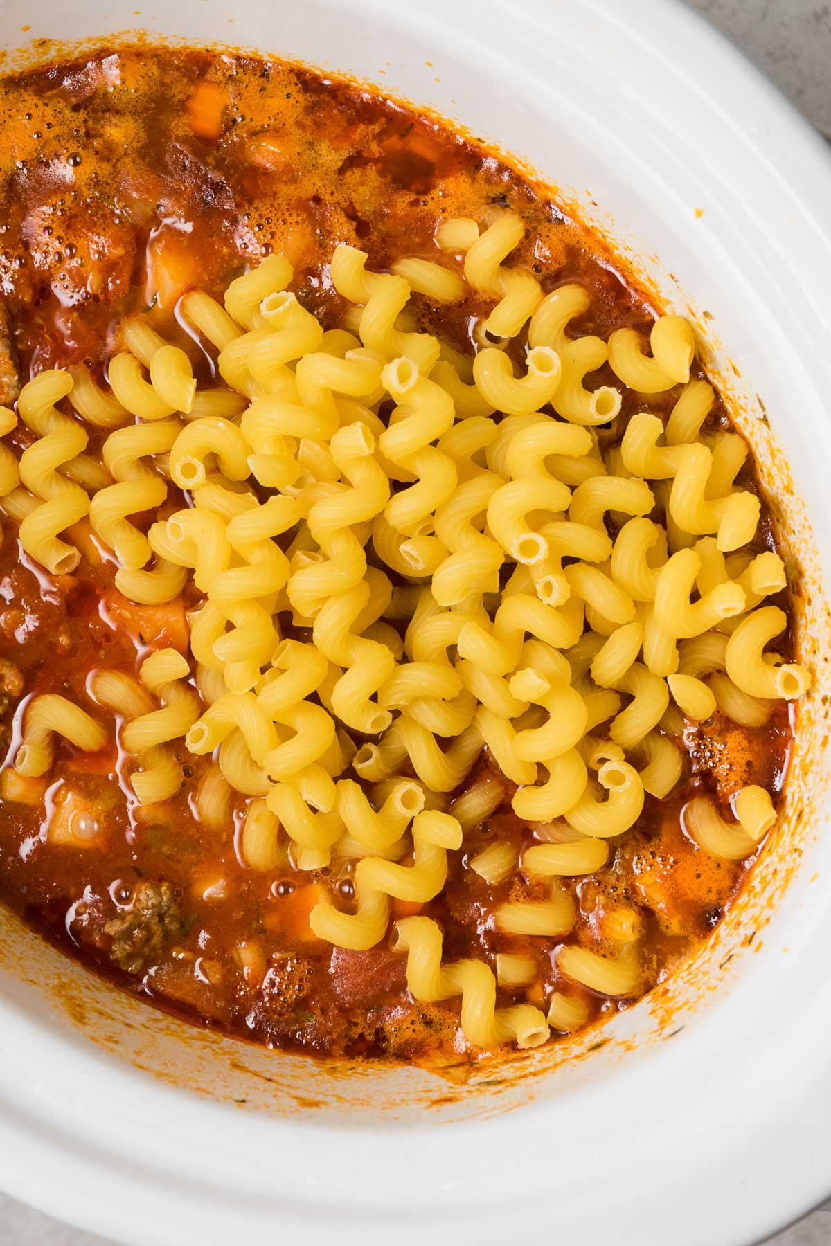 Spiral macaroni pasta is added to slow cooker goulash.