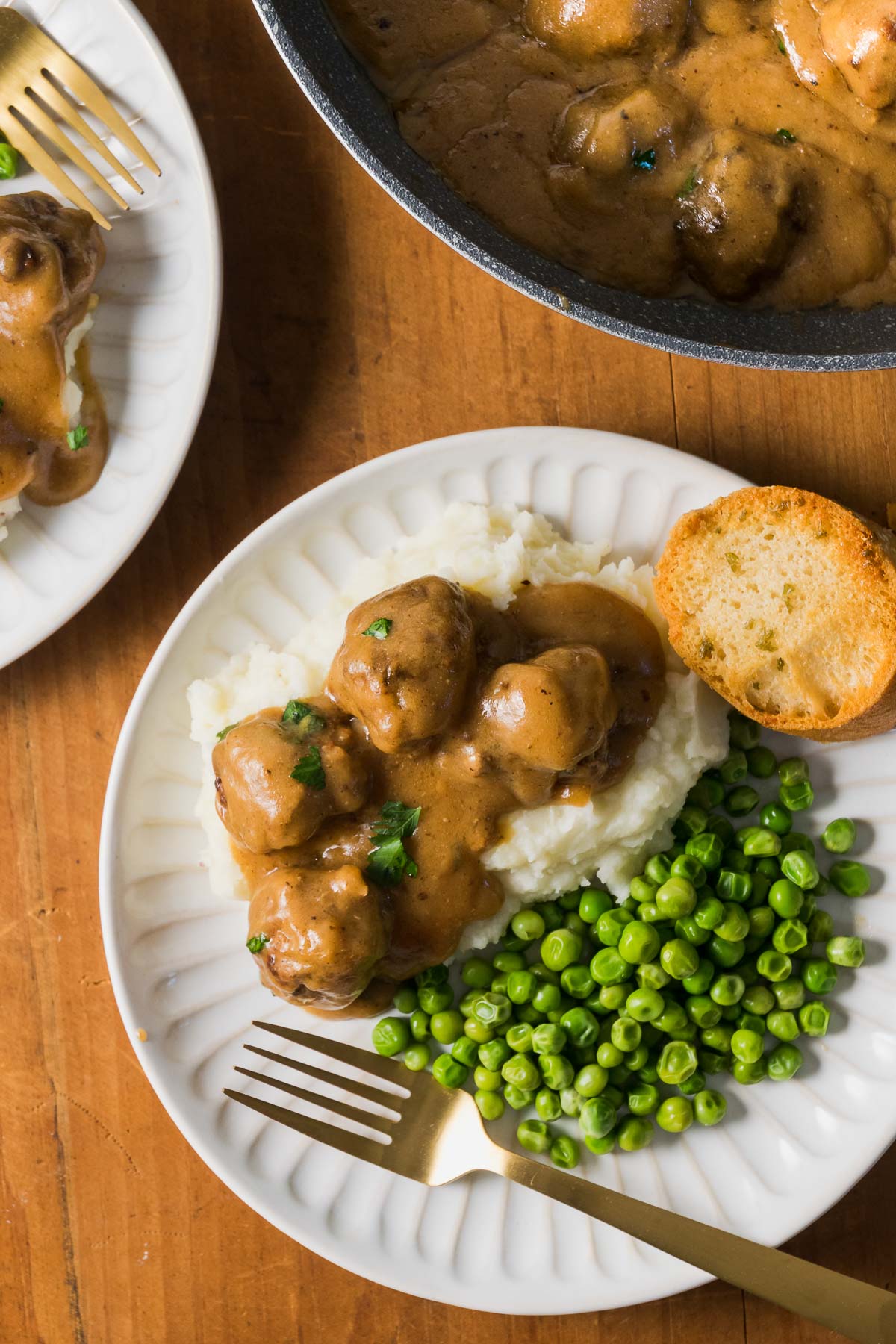 A dinner table set with plates of crock pot Swedish meatballs over mashed potatoes and peas.