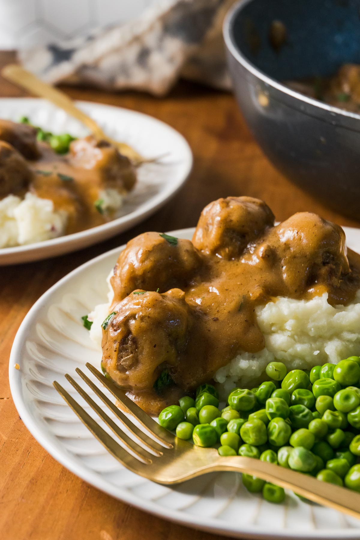 A dinner plate of crock pot Swedish meatballs, over mashed potatoes and peas.