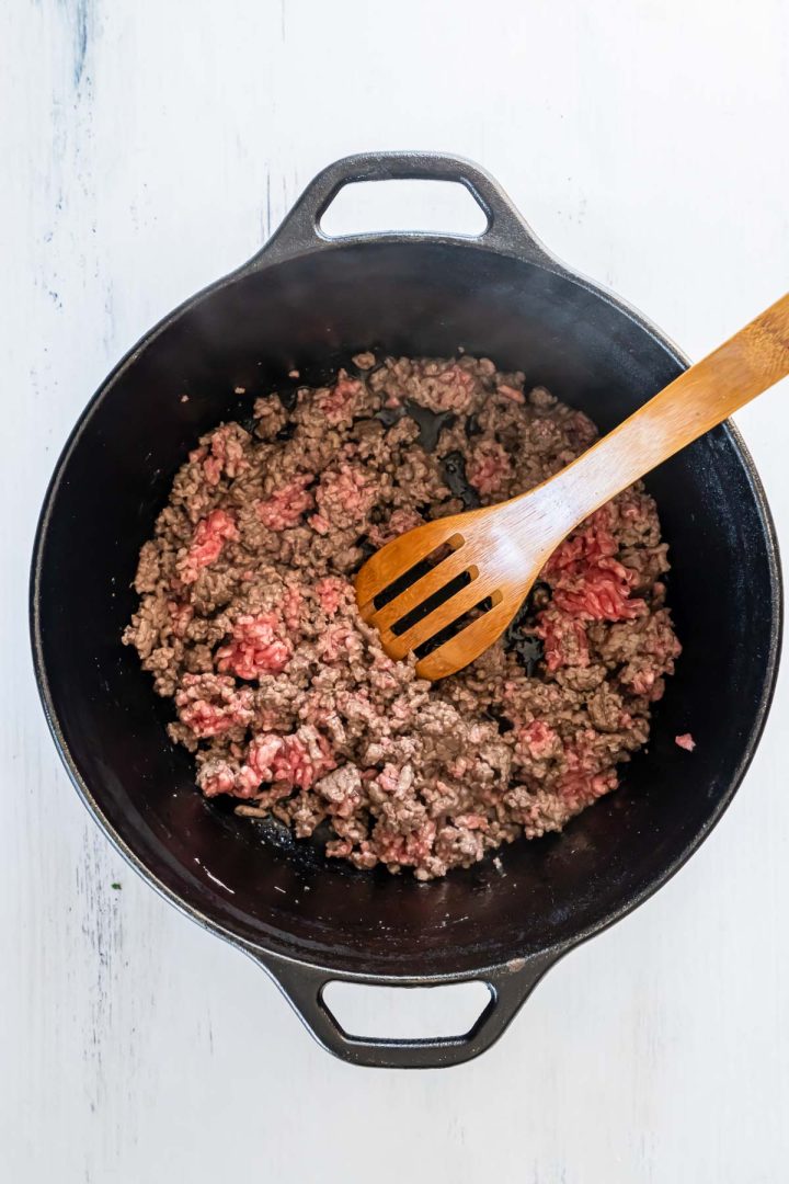 Sauteed ground beef being stirred with a wooden spoon.