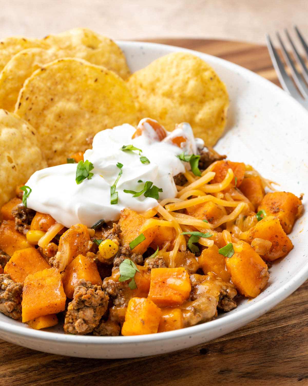 A bowl of Ground Beef and Sweet Potato Skillet Hash with sour cream and tortilla chips.