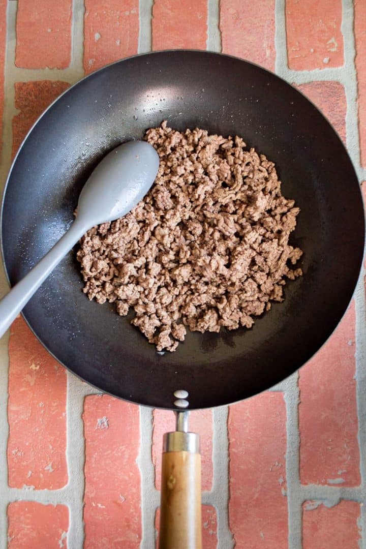 Cooked ground beef in a saute pan on a brick backdrop.