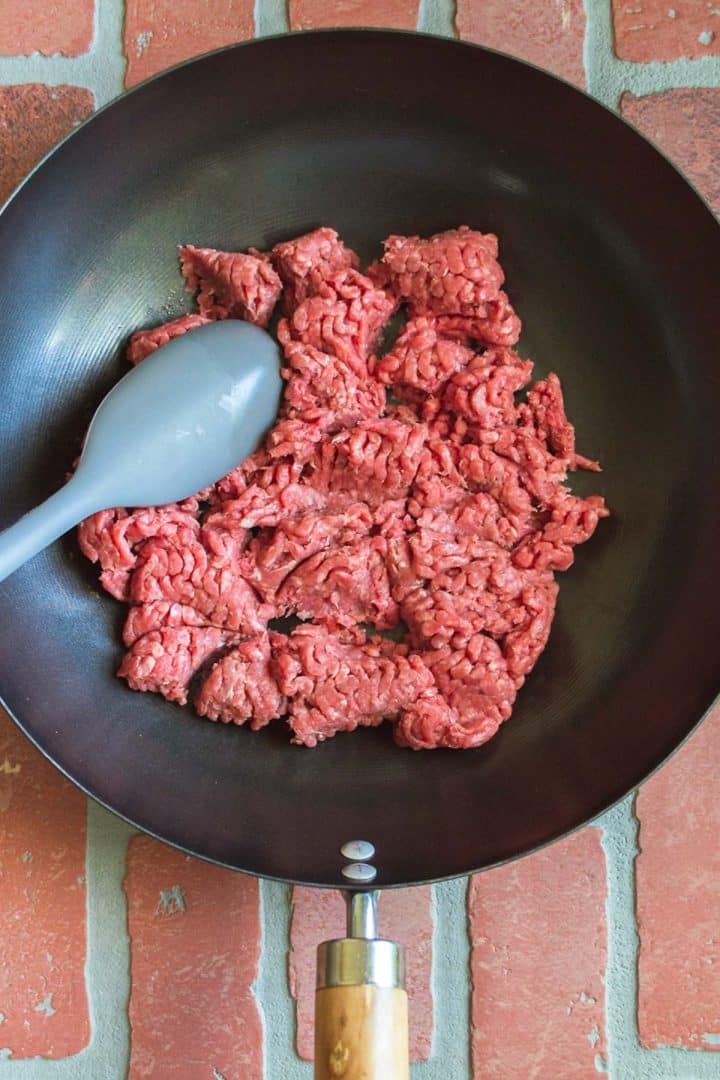 Raw ground beef in a skillet with a blue spoon.