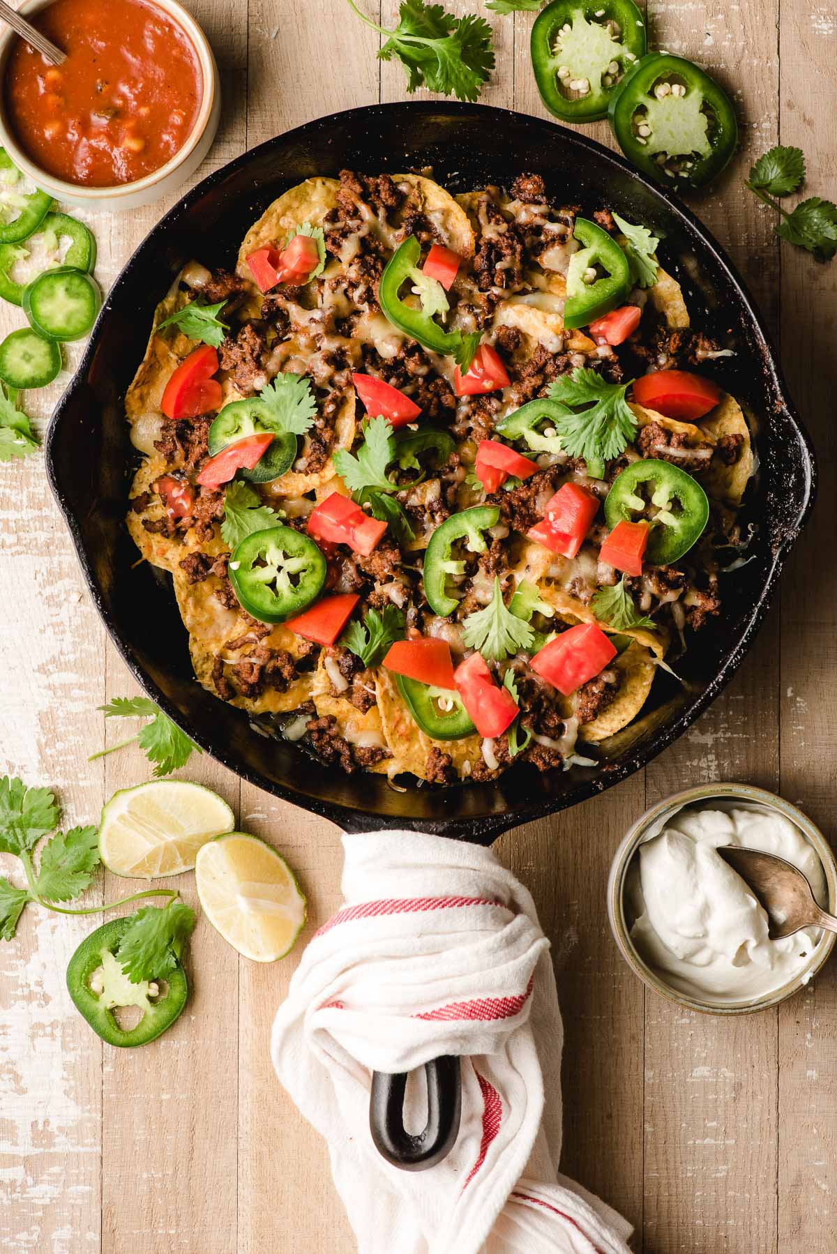 Cast Iron Skillet Nachos with Ground Beef, jalapenos, tomatoes, cilantro, and sour cream and salsa on the side.